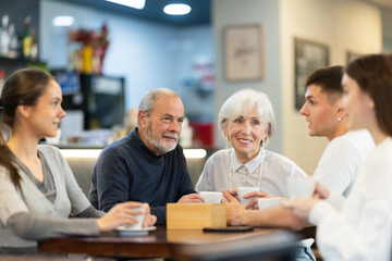 Meeting big family in cafe. Young and senior relatives chatting sweetly during tea party, discussing news, sharing their impressions. Shopping Mall food court - meeting place for friends.