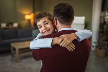 Happy boy hugging his father smiling at home