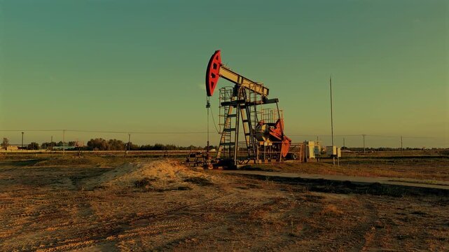 Oil Pump Jack Operates on Beautiful Sunset at Oil Field in Industrial Area. Crude pump jack working on sunrise in oil field. Oil drill rig, drilling derrick in oilfield. Crude petroleum industry. 