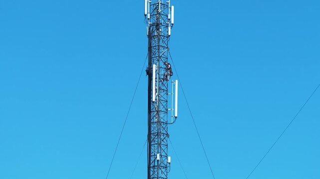 Two repairmen service a cell tower, install new cable and equipment. High-altitude work. Workers repair cell tower. Workers on mobile phone tower. Maintenance staff at work