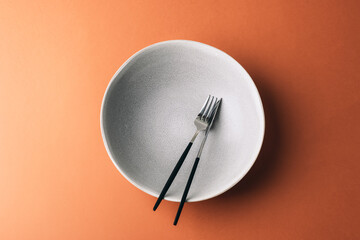 Empty grey plate with fork and knife on warm brown background. Top view, flat lay