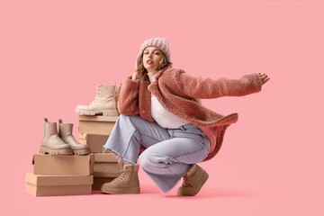 Stylish young woman with winter boots and shoe boxes on pink background