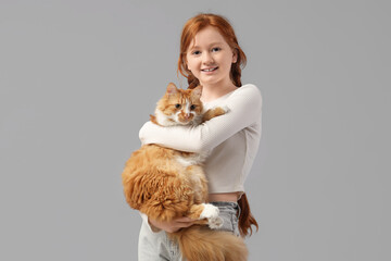 Redhead teenage girl with cute cat on grey background