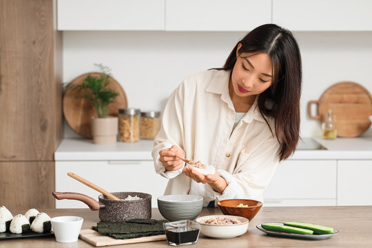Beautiful Asian woman preparing traditional Japanese onigiri with tuna in kitchen