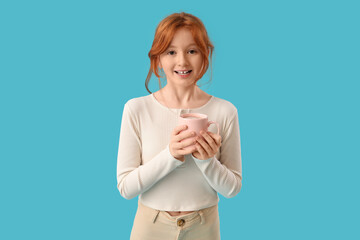 Teenage redhead girl with cup of sweet cocoa on blue background