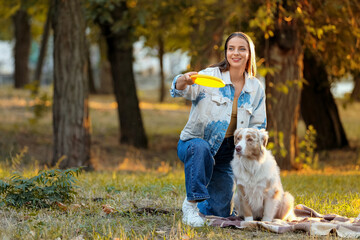 Fototapeta premium Young woman with cute Australian Shepherd dog playing frisbee in park