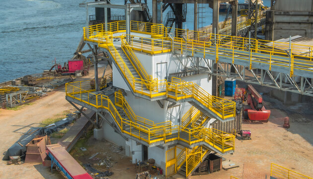 Industrial facility featuring a white building with vibrant yellow outdoor staircases and metal walkways at a maritime port construction site - Powered by Adobe