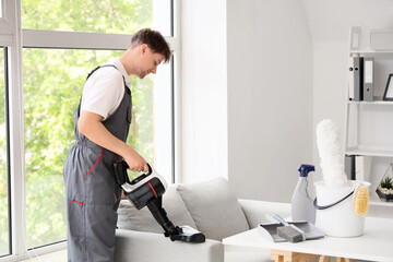 Young male janitor with modern handheld vacuum cleaner cleaning sofa in room © Pixel-Shot