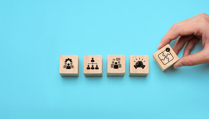 Wooden blocks showing icons of teamwork, leadership, communication, collaboration, and problem solving, with a hand placing a puzzle piece symbolizing strategic team development