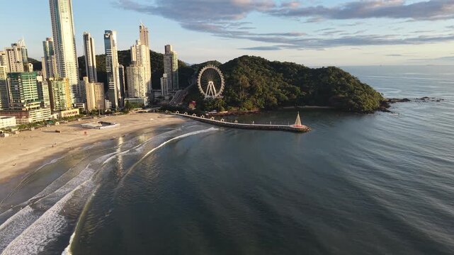 An eye-level shot captures a coastal city with skyscrapers alongside the serene sea, an observation wheel, and a lush mountain. 