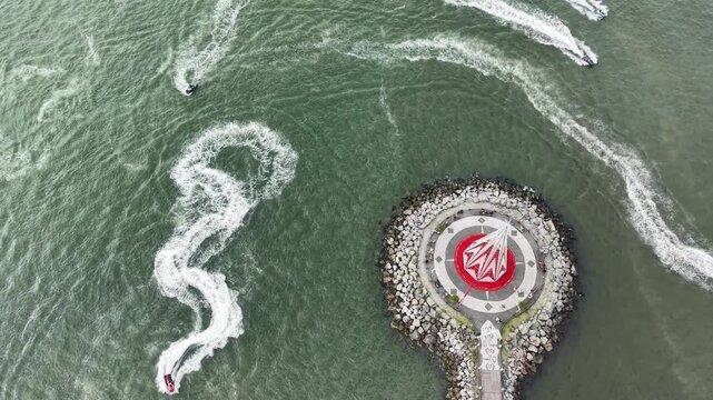 Aerial view of jet skis creating patterns on the water near a navigational marker. 