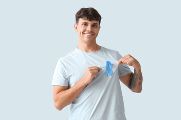 Young man with blue ribbon on light background. Prostate cancer awareness concept