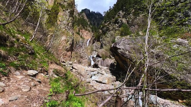 Shagatsikomdon Waterfall, in the spring in the Caucasus Mountains. Mountain landscape. Waterfall in the Tsey Gorge. North Ossetia-Alania, Russia. A multi-stage 15-meter waterfall in the sunlight. 4К
