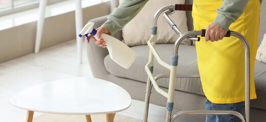 Mature woman with walker cleaning table in room