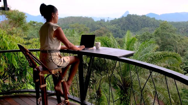 Relax in Khao Sok, Thailand, where lush greenery meets stunning mountains. Enjoy a serene workspace with breathtaking views, a woman working on a laptop in nature at a bunglow terrace