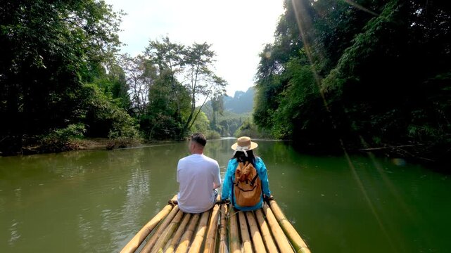 Two travelers enjoy a relaxing moment on a bamboo raft, gliding through the serene waters of Khao Sok, Thailand. Surrounded by stunning greenery and towering cliffs, natures beauty shines.