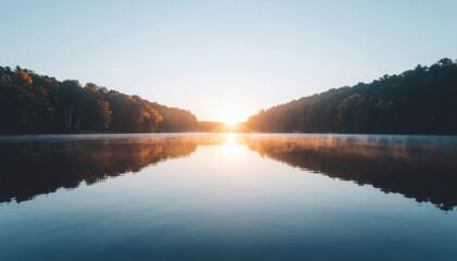 Serene lake at sunrise with trees reflected on calm water surface against clear blue sky.
