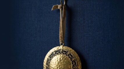 Decorative golden ornament hanging against deep blue background with subtle texture