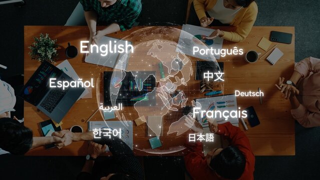 A diverse group collaborates around a wooden table, with laptops and notebooks illuminated by a digital world map highlighting various languages, symbolizing global communication. Raster