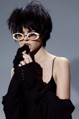 Stylish woman with short dark hair and white sunglasses wearing black, posing confidently with a modern and edgy look