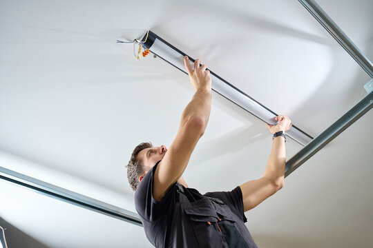 Man in workwear installing a linear LED light fixture on the ceiling indoors. Concept of electrical installation, maintenance work and home renovation.