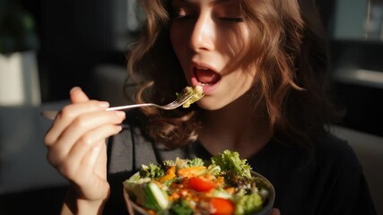 A close up of a woman savoring a colorful salad, emphasizing wellness and balanced nutrition. Sunlight enhances the freshness and appeal of the healthy food choice in a modern setting