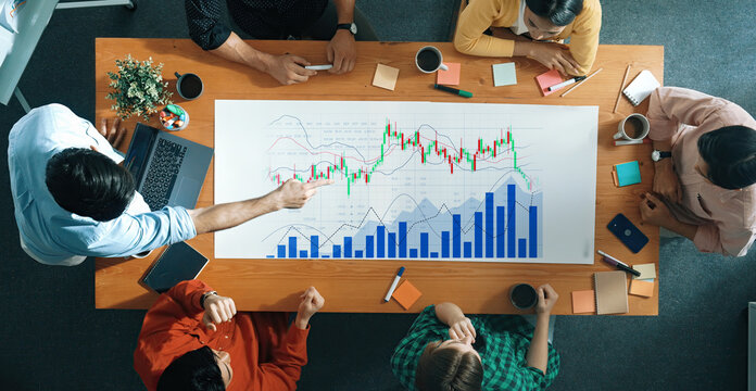 A diverse group of professionals collaborates in a modern office, analyzing market trends with graphs and charts on a table, highlighting teamwork and strategy. Scalp - Powered by Adobe