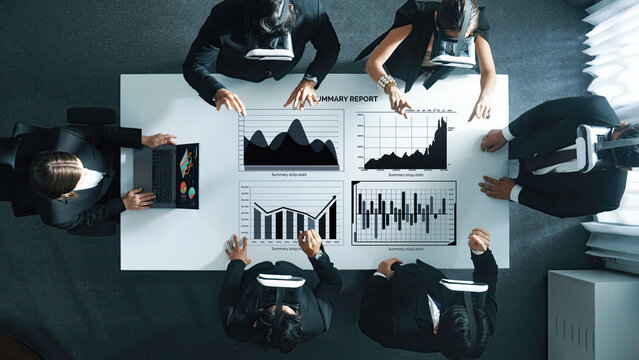 A business team engages in a meeting utilizing virtual reality technology to analyze financial data through interactive digital charts, promoting collaboration and insight. Axiom - Powered by Adobe