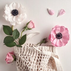 Overhead shot displays a string net holding pink roses and greenery. Two anemone blossoms and petals are on a white surface