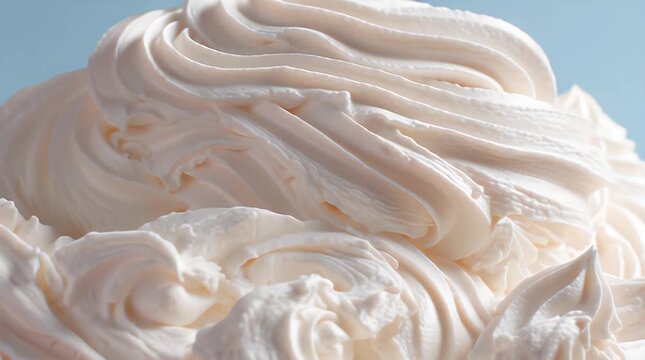 A close-up view presents swirls of a pale, creamy confection with visible textures. The soft, textured surface contrasts with a muted blue backdrop