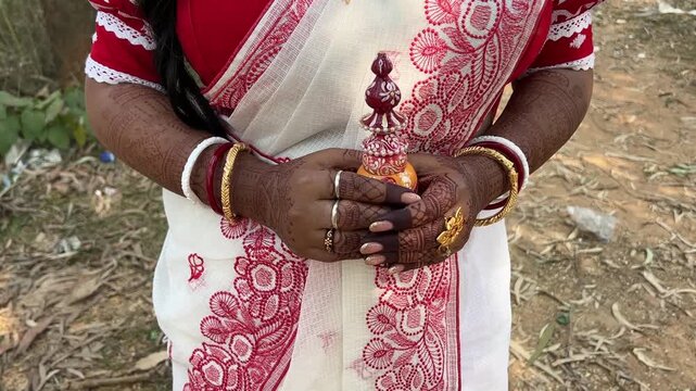 A Bengali bride in red and white saree standing outdoor holding a sindur box for wedding in India