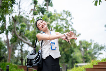 Naklejka premium Asian woman office worker holding phone closing eyes stretching hands or arms while standing in park