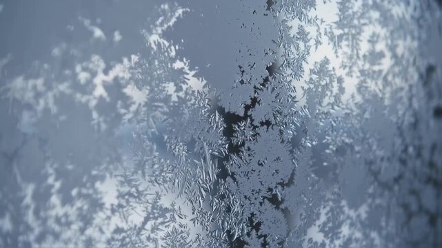 Intricate frost patterns adorn a window, with crystalline formations and blurred highlights, creating a cool ambiance