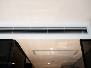 Wall-mounted air vent system inside a white clean modern hotel room, showing HVAC ductwork for...