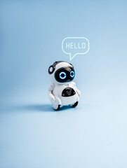 Cute futuristic robot toy with glowing eyes and speech bubble saying “HELLO” isolated on blue background, representing AI assistant, chatbot technology, digital communication, and virtual support. © tete_escape