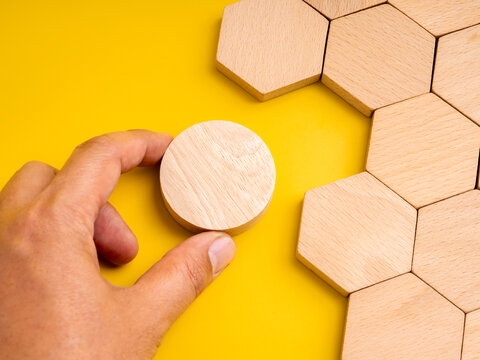 Concept of mismatch and problem solving with hand holding a round wooden piece not fitting into hexagon space. Symbolizes difference, challenge, creativity, unique thinking, and solution development.