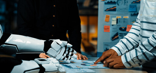 A robot and a human engage in a collaborative office meeting, discussing data analysis and presenting charts, showcasing the integration of technology and business strategy.Noogenesis