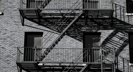 Dramatic monochrome capture of a multi-tiered metal fire escape creating sharp, angular shadows across a classic brick building in an urban setting