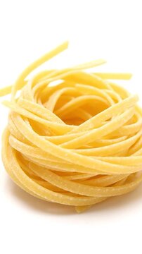 Close-up of yellow pasta nest on white background, composed of many strands