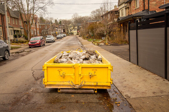 Yellow construction dumpster filled with broken concrete placed on a residential street in Toronto&rsquo;s Beaches neighbourhood during winter, showing urban renovation, demolition waste, and residential bu