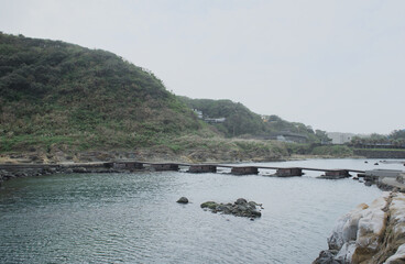 Scenic stone bridge walkway crossing the crystal clear coastal water at Heping Island Park, Keelung, Taiwan.