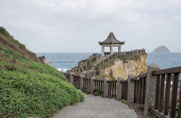 Traditional Chinese pavilion and concrete pathway along the coastal cliffs at Heping Island Park with Keelung Islet in the distance, Taiwan.