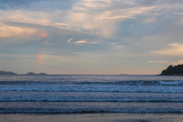 reflexo do c&eacute;u e o p&ocirc;r-do-sol na Praia Palmas do Arvoredo cidade de Governador Celso Ramos Santa Catarina Brasil regi&atilde;o da Grande Florianopolis  ao fundo um arco-&iacute;ris na costa de Bombinhas  Mariscal  