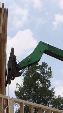 Workers are assembling structure with telehandler crane lifting wooden beams under bright sky with clouds