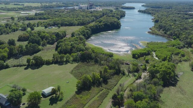 Riverside homes and green fields near industrial power generation site and lake, aerial overview