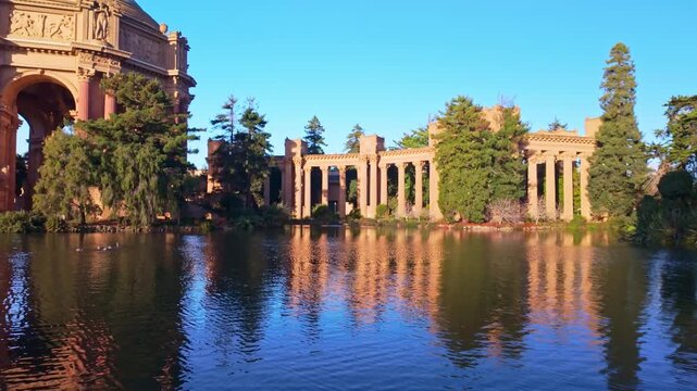 Classical Roman style rotunda and colonnades reflected in the calm lagoon during a vibrant golden sunrise in San Francisco