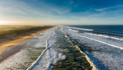 Aerial view of a vast, pristine beach with foamy waves stretching into the horizon under a clear sky.