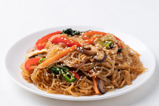 Japchae, Korean stir fried glass noodles with vegetables, pork, soy sauce and sesame oil on white background