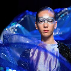 Futuristic model with metallic eye makeup and glowing blue fabric, embodying avant-garde fashion, sci-fi aesthetics and digital runway energy.