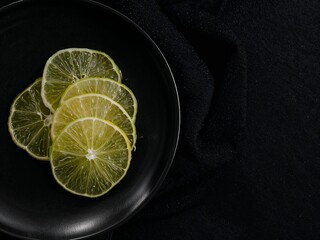 Sliced lime in black bowl on dark background, minimal food styling with copy space, fresh citrus concept.